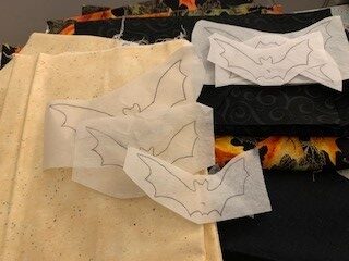 Halloween-themed fabrics with appliqué bat shapes traced on fusible web, ready for cutting.