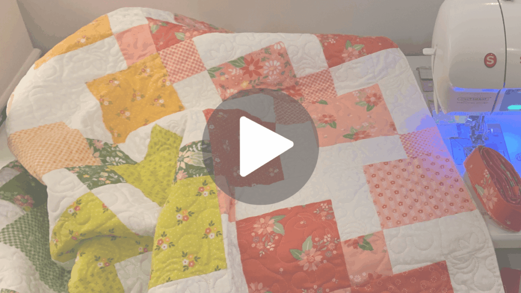 Link to short video showing the full view of Gia’s Color Wash Disappearing 9-Patch baby quilt, with bright red, coral, yellow, green, and teal squares displayed in natural light.