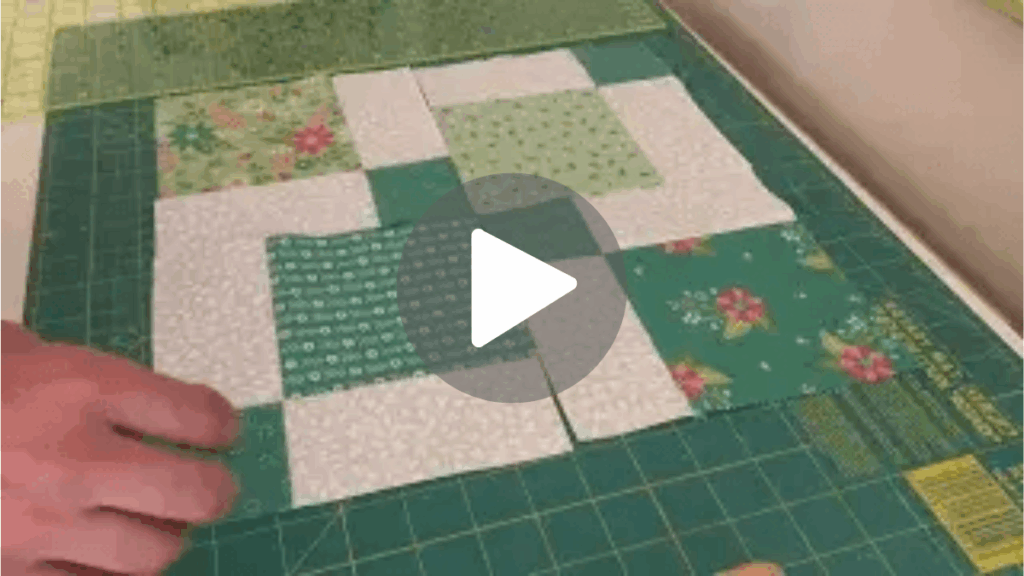 Video player link with hands arranging green and white fabric squares into a disappearing nine-patch quilt block on a cutting mat.