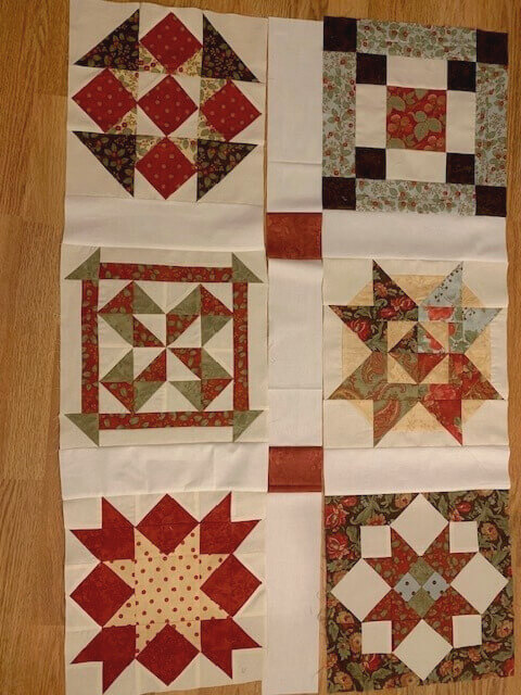 Christmas Block of the Month quilt blocks laid out with cream sashing and red cornerstones during layout planning.
