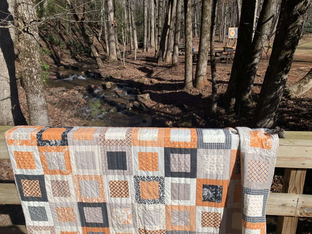 Fall Framed Windows quilt displayed along a wooden railing near a creek