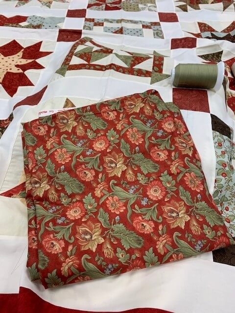Red floral backing fabric and green thread laid across quilt top