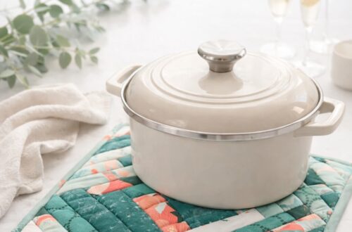 Quilted log cabin casserole hot pad in teal and green fabrics holding a covered casserole dish on a light kitchen counter.