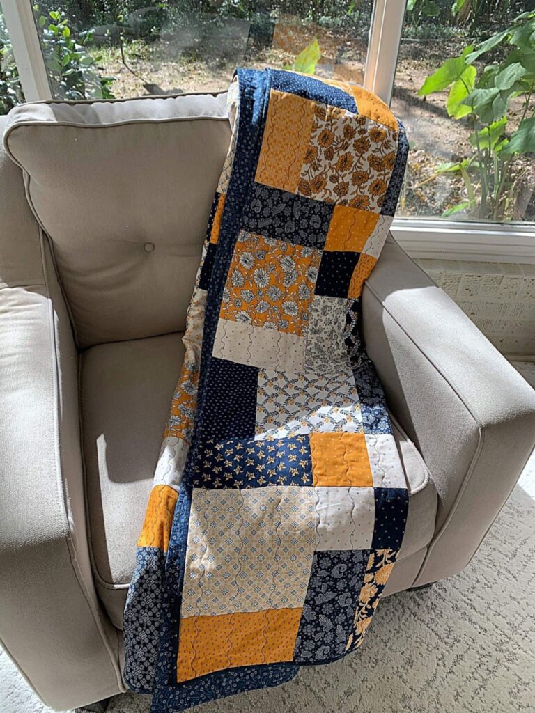 Layer cake loop quilt draped over an armchair near a window.