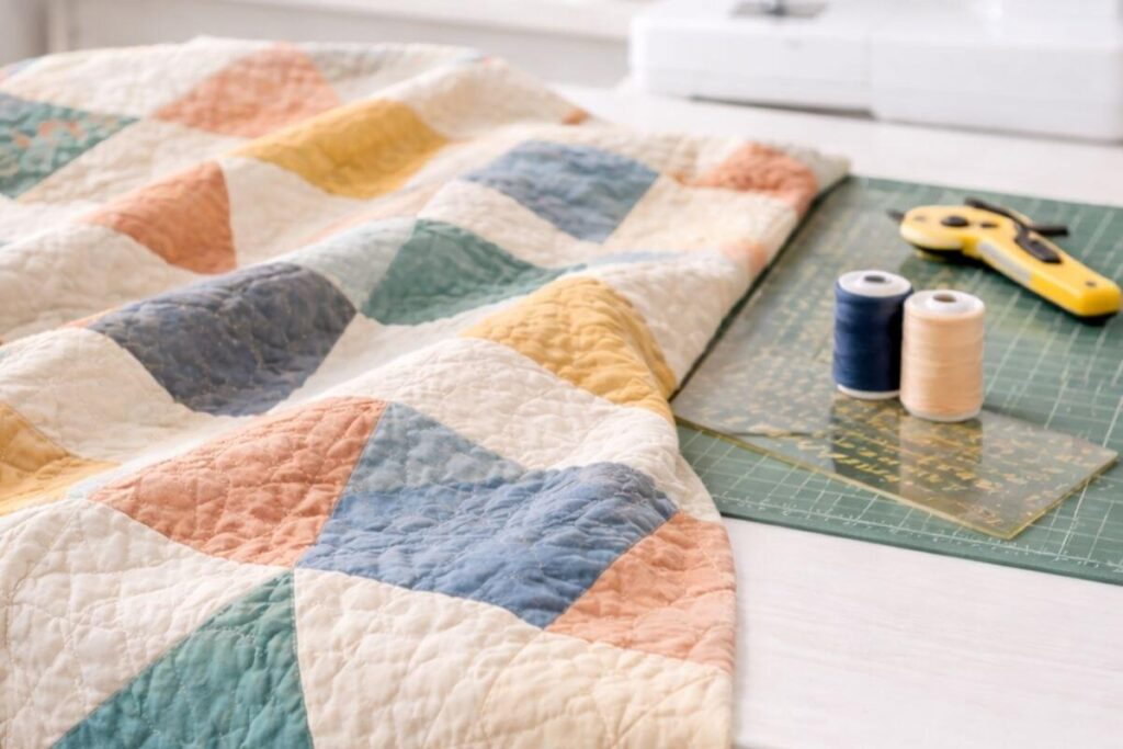 Partially finished quilt draped over a table with thread spools and quilting tools